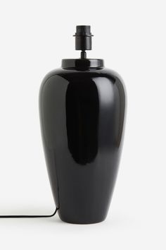 a black vase sitting on top of a white table next to a light bulb and cord