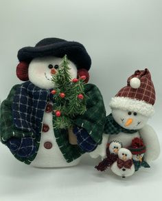 two snowmen with hats and scarves are holding a small christmas tree in their hands