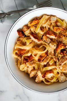 a white bowl filled with pasta and meat on top of a marble table next to utensils