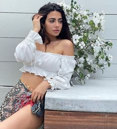 a beautiful woman sitting on top of a wooden bench next to white flowers and greenery