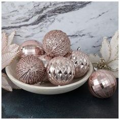 some shiny pink ornaments are on a white plate next to leaves and marble wallpaper