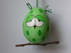 a green painted egg sitting on top of a tree branch with eyes drawn on it