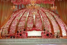 an elaborately decorated stage with pink flowers and chandelier hanging from the ceiling