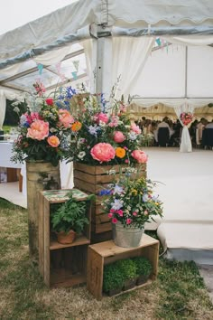 flowers are arranged in wooden crates on the grass near a white tent and tables with chairs