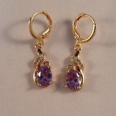 These Beautiful Purple Topaz Ribbon Swirl Earrings Are Made Of 18k Yellow Gold Filled. The Large Oval Topaz Zircon (Lab Created) Stones Are 6x8mm And With A Swirl Of Smaller White Topaz Stones. Brand New And Never Been Worn. Lead And Nickel Free. These Fine Quality Earrings Are Perfect And Comfortable For Special Occasions Or A Special Gift. Please Send Offers And Questions. Big Stone :6 X 8mm Or .24" X .31" Earrings: 1.22" X .31" Fastening: Hoop Clasp (Pierced) Hoop Diameter: .47" Amethyst Earrings Gold, Purple Drop Earrings, Purple Amethyst Earrings, Purple Gems, Swirl Earrings, Amethyst Jewelry, Topaz Stone, Purple Stones, Amethyst Earrings