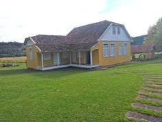 a small yellow house sitting on top of a lush green field