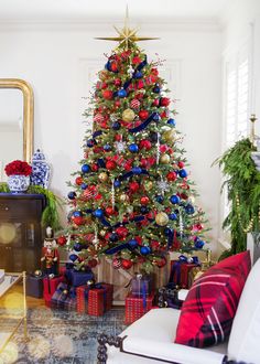 a christmas tree decorated with red, white and blue ornaments in a living room area