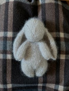 a knitted stuffed animal sitting on top of a plaid cloth covered bed spreader