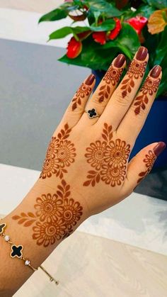 a woman's hand with henna tattoos on it and flowers in the background