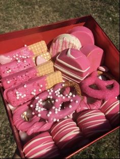 a red box filled with lots of pink and white desserts on top of grass