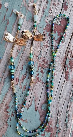 a necklace with dragonfly charms and beads on a piece of weathered wood, next to an earring