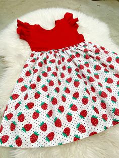 a red and white dress with strawberries on it sitting on a furnishing