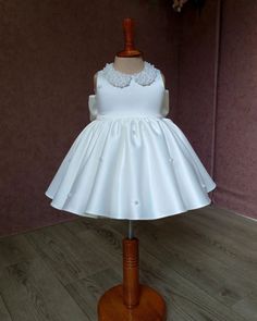 Your little one will look absolutely adorable in this ivory baby girl dress! Featuring a pearl-adorned neckline and a soft, puffy design, it's perfect for weddings, birthdays, and special celebrations. Made from gentle, breathable fabric, it keeps your child comfy all day. Whether as a flower girl dress or a party outfit, this timeless piece adds elegance to every memorable moment. ----DETAILS---- > Knee Length > Peter Pan Collar > Sleeveless -----COLOR----- If you want the dress in a custom col Elegant Dresses With Pearl Embroidery For Formal Occasions, Elegant Tutu Dress With Satin Bow For Baptism, Princess Style Satin Dress For First Communion, White Princess Dress With Pearl Embroidery, Sleeveless Satin Princess Dress, Satin Sleeveless Princess Dress For Dress-up, Sleeveless Satin Princess Dress For Dress-up, Sleeveless Satin Princess Dress For Pageant, Elegant Sleeveless Pageant Dress For Baptism