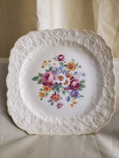 a plate with flowers painted on it sitting on a white tablecloth covered table cloth