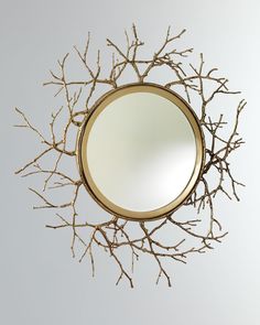 a round mirror with branches hanging from it's sides and a gold frame on the wall