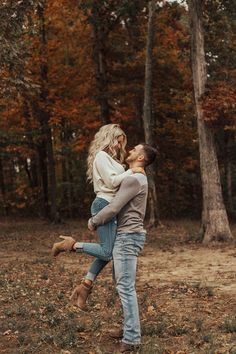 a man holding a woman in his arms while they are walking through an autumn forest