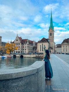 a woman standing on the side of a river next to buildings