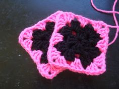 two pink and black crocheted squares sitting on top of a table