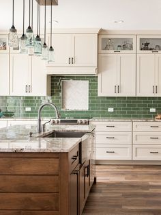 a kitchen with white cabinets and green glass tile backsplash, wood flooring