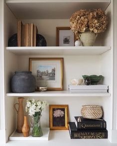 some books and vases are sitting on the shelves in a room with white walls