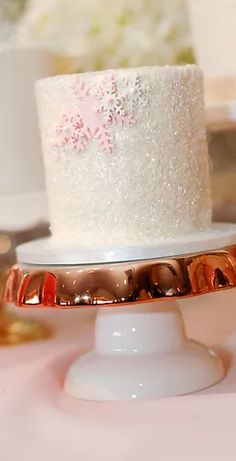 there is a white cake with pink flowers on the top and gold trimmings