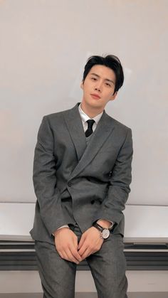 a man in a suit and tie sitting on a bench with his hands clasped to his knees