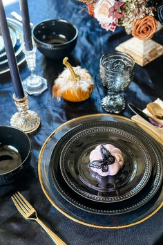 a table set with black and gold place settings, silverware, pumpkins and candles