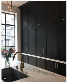 a kitchen with black cabinets and marble counter tops, gold faucet, and a large window