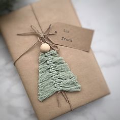 a wrapped christmas tree ornament on top of a brown gift box with a tag