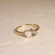 two stone ring sitting on top of a white surface with gold trim around the band