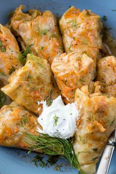 a blue bowl filled with dumplings covered in sauce and garnished with sour cream