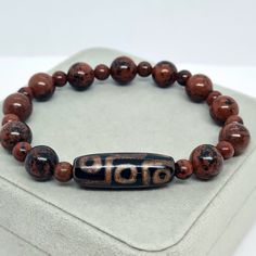 Agate Tibetan Dzi bead bracelet with Red Obsidian stone beads. Lucky amulet for a gift. Bracelet size made to order. Please send me the size of your wrist so the bracelet will fit perfectly. Bead size: Dzi - 3×1 cm/1.16×0.42 inches. Bronzite - 6 and 11 mm/0.24 and 0.4 inches. If you choose to pack No.2, leave me a message about which stamp you would like (Crown, Cloverleaf, Just Smile). I will choose the color of the stamp at my discretion if you do not have any other wishes 🙂 You may also want Red Agate Beaded Bracelets For Meditation, Red Agate Beaded Bracelet For Meditation, Spiritual Beaded Bracelets With Natural Stones For Good Luck, Amulet Bracelet With Round Beads For Gift, Brown Agate Beaded Bracelet With Polished Beads, Amulet Style Bracelet With Round Beads As Gift, Spiritual Obsidian Beaded Bracelets With Natural Stones, Hand-strung Obsidian Beaded Bracelets As Gift, Spiritual Healing Bracelets With Oval Beads