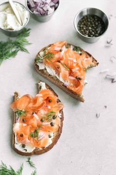 two pieces of bread with salmon and cream cheese on them next to bowls of vegetables