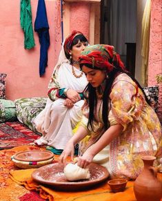 two women are making bread on the floor in front of a pink wall and rug