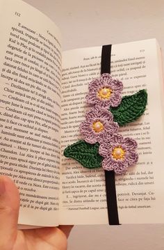 a hand holding an open book with crocheted flowers on it