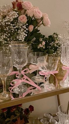 many wine glasses are sitting on a table with pink ribbon and flowers in the background