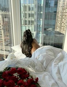 a woman laying in bed with her head on the pillow next to a bouquet of roses