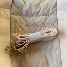 a white and pink bag with some gold hooks on it's side, next to the name rare beauty