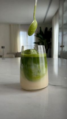 a green liquid in a glass with a spoon sticking out of the top, on a white countertop