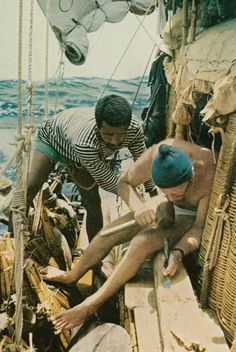 two men working on a boat in the ocean while another man watches from the deck