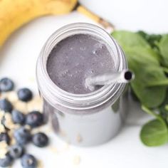 a glass jar filled with blueberries next to a banana and spinach leaves on a white surface