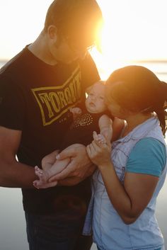 two adults and a child are standing by the water with their hands around each other