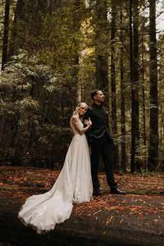 a bride and groom standing on a log in the woods