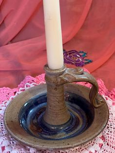 a white candle is sitting in a bowl on a doily with a pink background