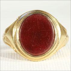 a gold ring with a red stone in the center on a white cloth covered surface