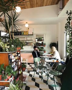 two people sitting at tables in a small room with potted plants on the walls