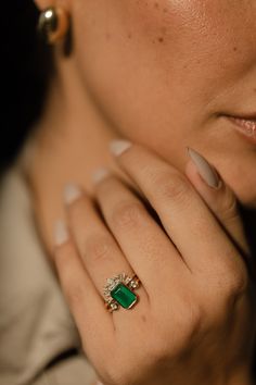 a close up of a person wearing a ring with a green stone on it's finger