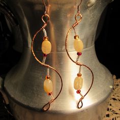 a pair of earrings with beads and wire wrapped around them on top of a metal stand