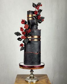 a three tiered black cake with red flowers on top and gold trimmings