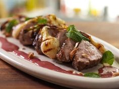 a white plate topped with meat covered in sauce and garnished with green leaves